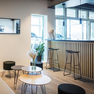 Helle Studio-Lounge mit Hochtresen, Barhockern, kleinen runden Tischen und Deko-Pflanzen.