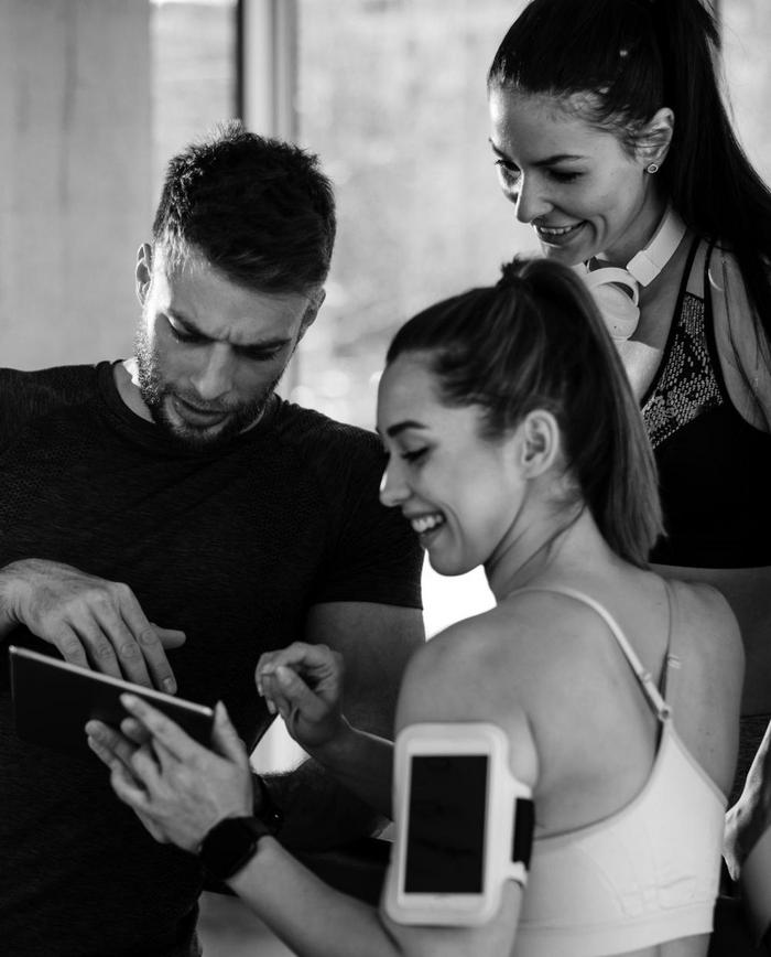 Drei Personen im Fitnessstudio schauen gemeinsam auf ein Tablet.