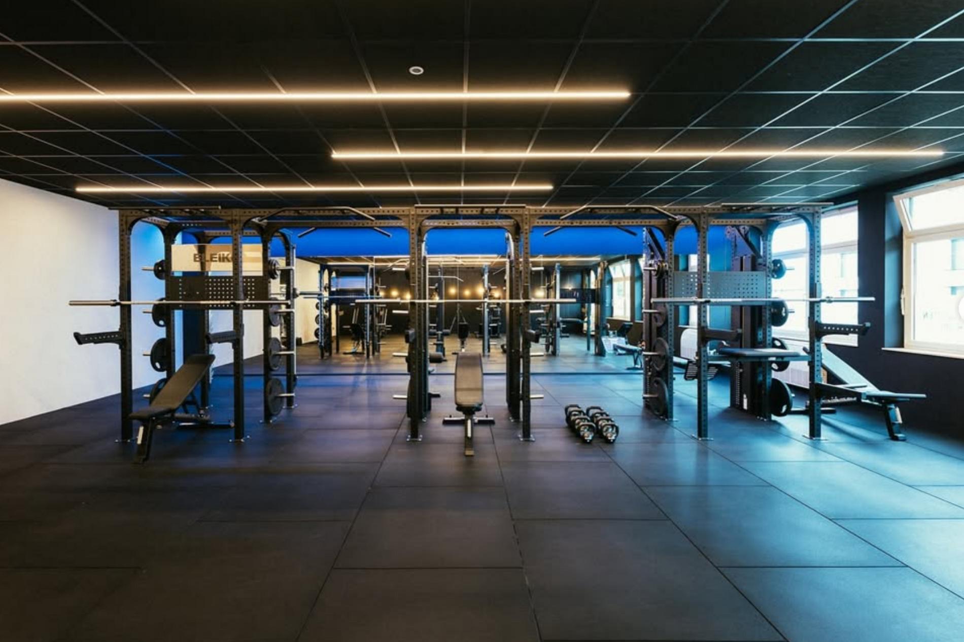 Großer Kraftbereich im Fitnessstudio mit mehreren Langhantelstationen und Hanteln.