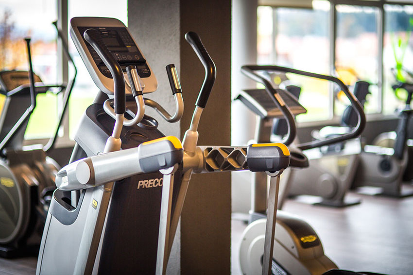 Cardiogeräte in einem hellen Fitnessstudio, im Vordergrund ein Crosstrainer.