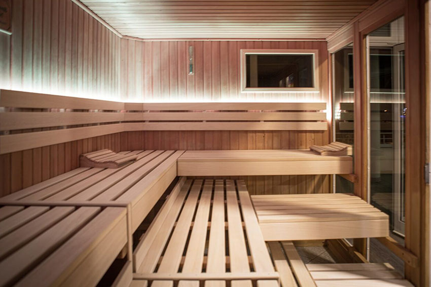 Moderne Sauna aus hellem Holz mit mehreren Sitz- und Liegebänken und indirekter Beleuchtung.