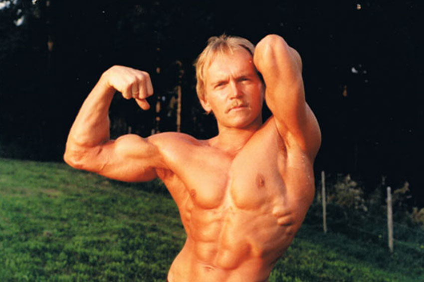 Bodybuilder steht outdoor auf einer Wiese und zeigt eine klassische Muskelpose.