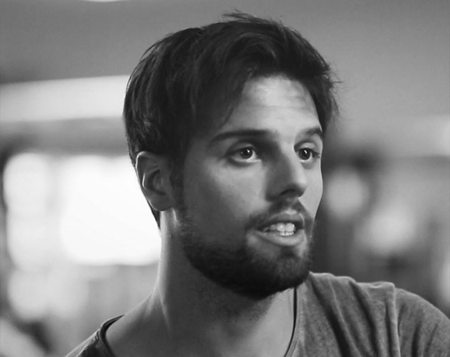 Mann mit Bart und kurzen Haaren spricht in einem Fitnessstudio.