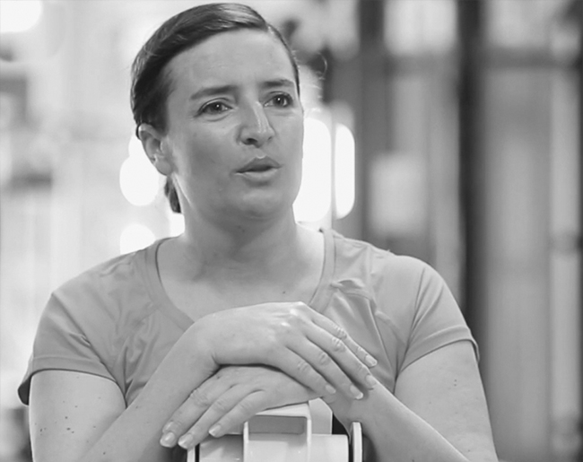 Frau im Sportshirt lehnt sich auf ein Trainingsgerät und spricht im Fitnessstudio.