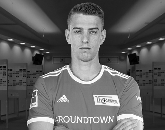 Fußballspieler im Union-Berlin-Trikot mit verschränkten Armen in einem Presseraum.